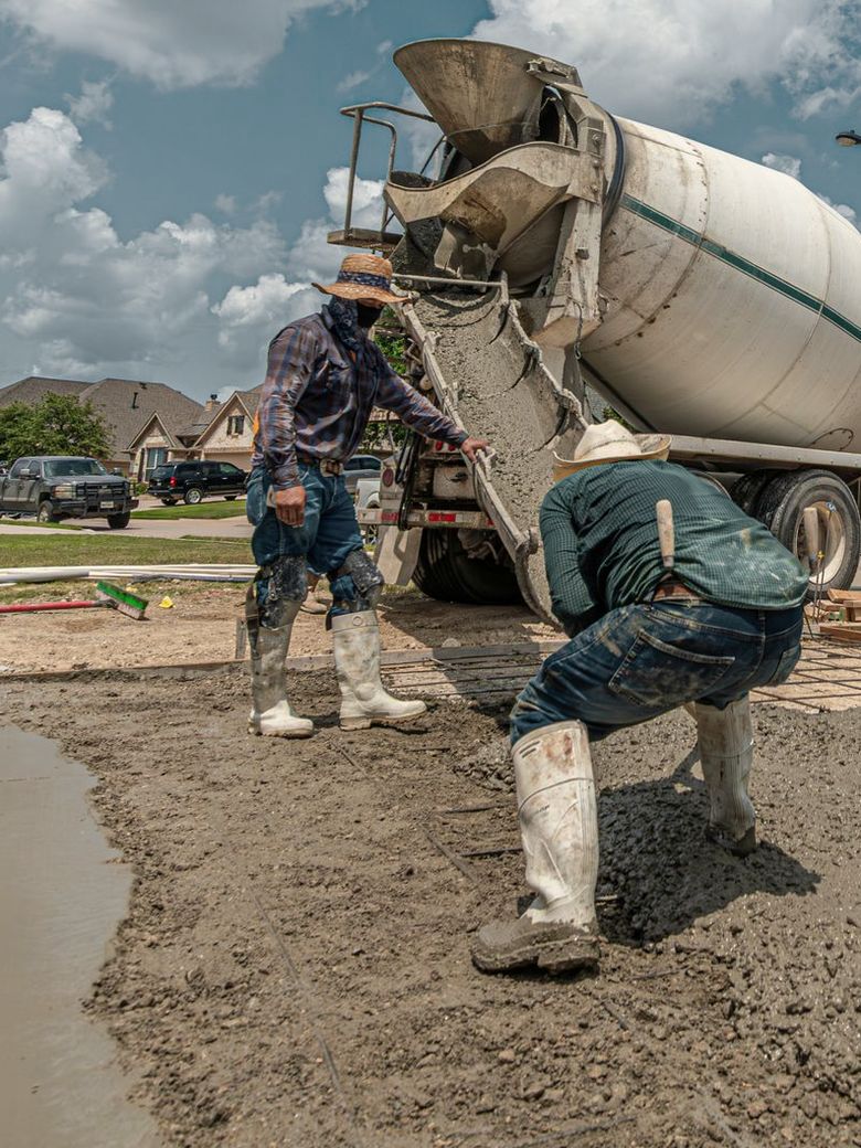 Crew pouring a new concrete driveway from a mixer truck in a residential neighborhood