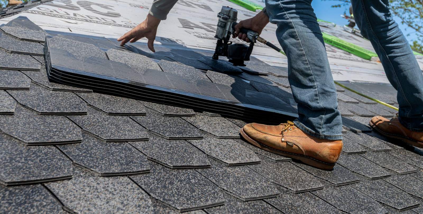 Roofer nailing new asphalt shingles on a pitched roof